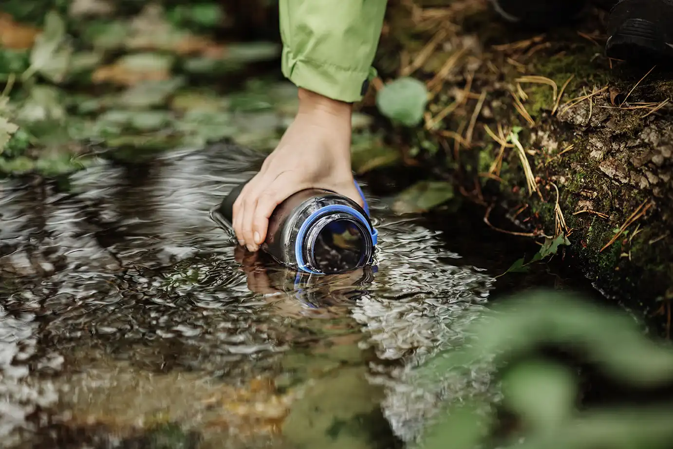 Randonneuse qui plonge une gourde dans l'eau